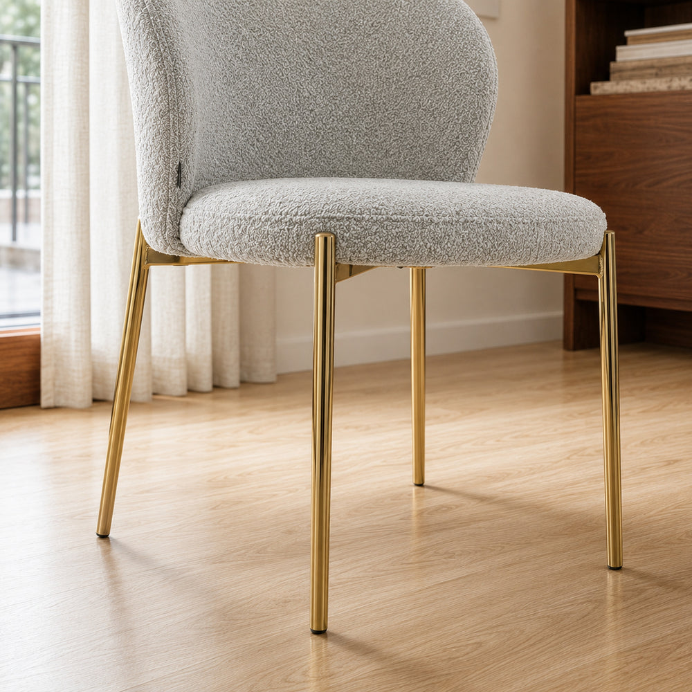 Detalle de las patas metálicas doradas y la base del asiento tapizado en tela bouclé gris.