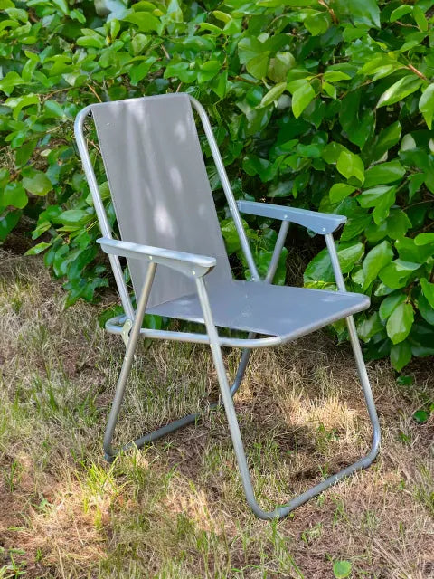 Reposera de lona coversol gris y estructura metálica ubicada en un jardín con vegetación de fondo.