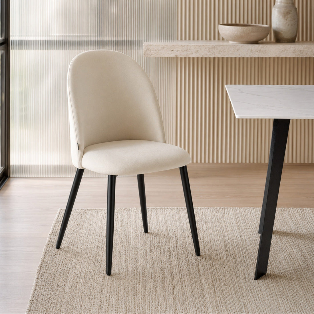 Silla Livia Lisa tapizada en pana beige con patas metálicas negras, vista de tres cuartos en comedor.
