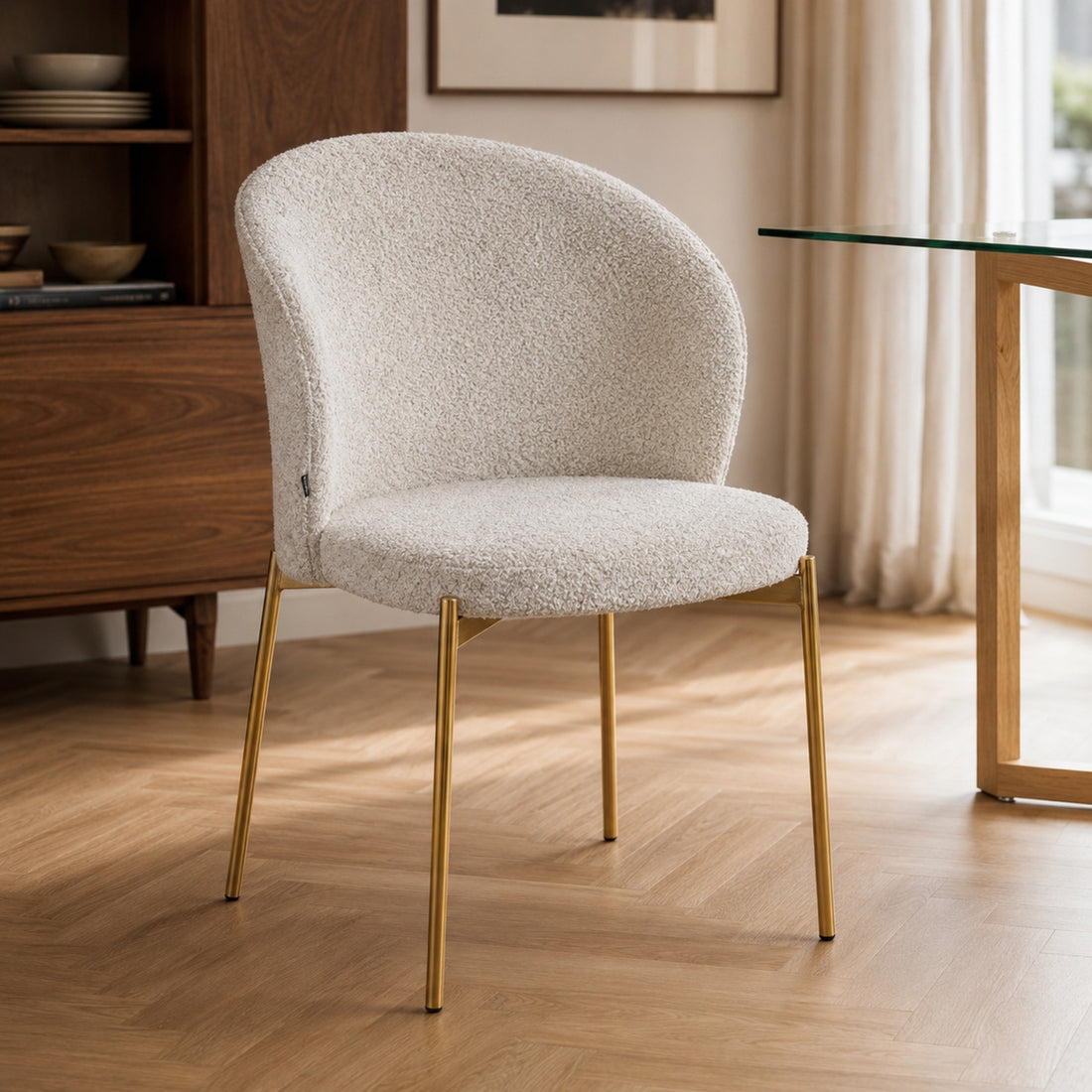 Silla Elira con tapizado bouclé beige y base dorada en vista de tres cuartos en un ambiente moderno.