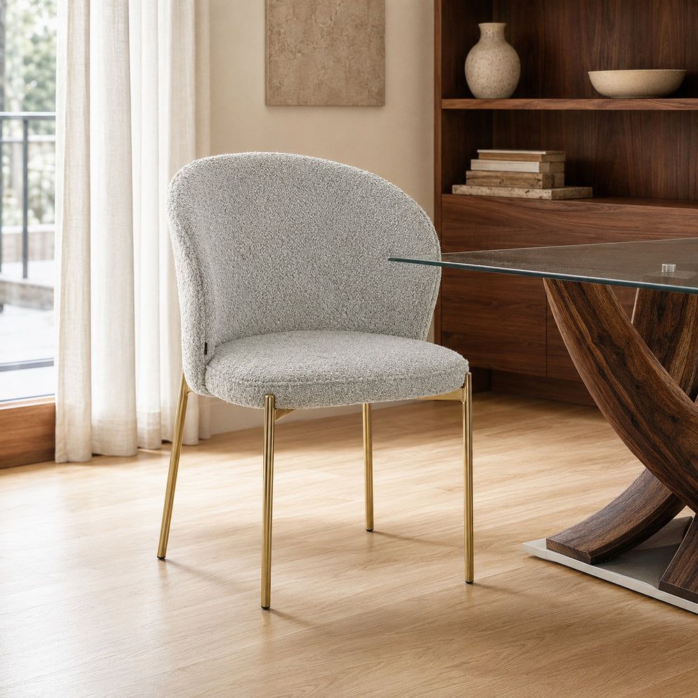 Silla Elira tapizada en bouclé gris claro con base dorada metálica en un ambiente de comedor.
