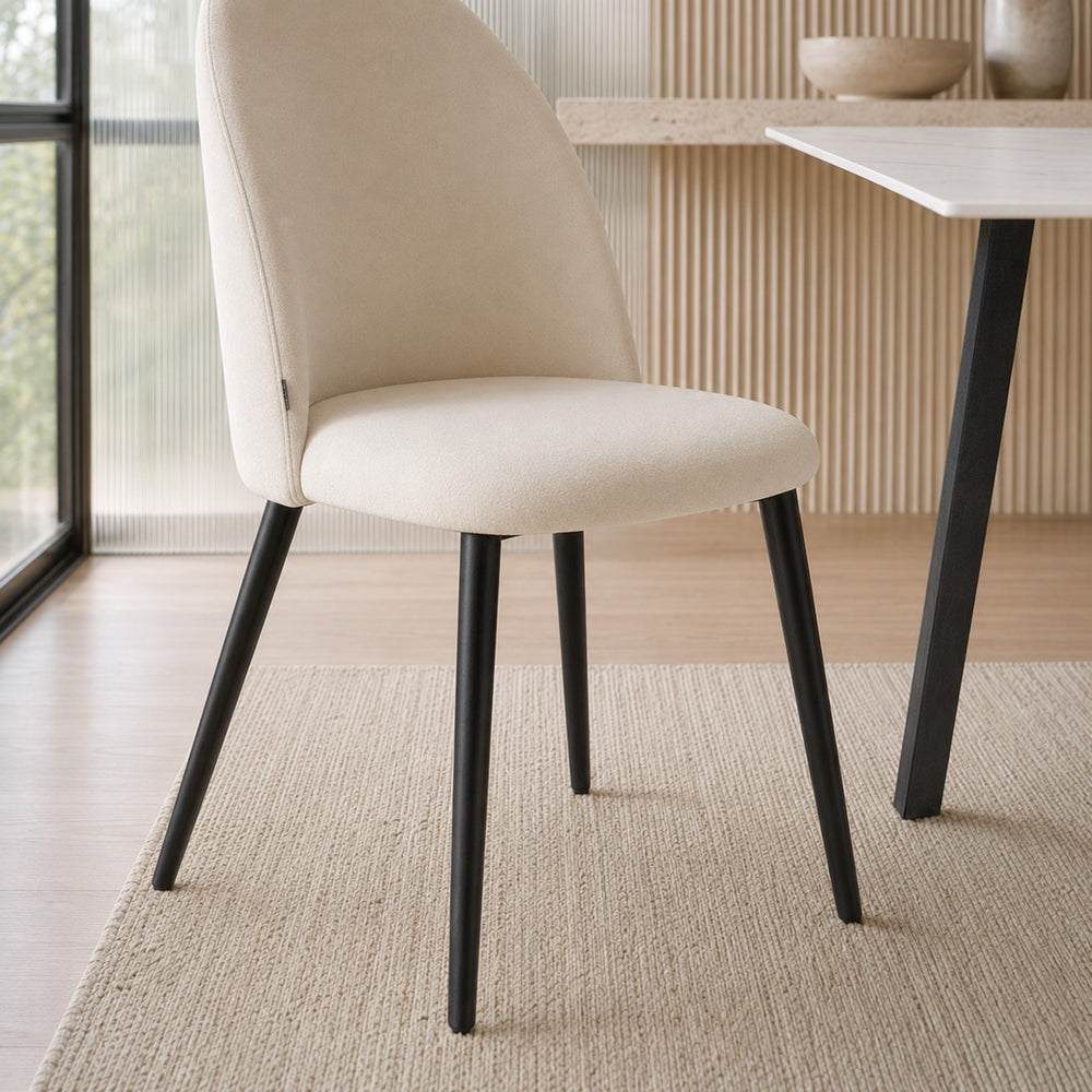 Primer plano de la silla Livia Lisa beige desde un ángulo bajo, mostrando el asiento y patas negras.