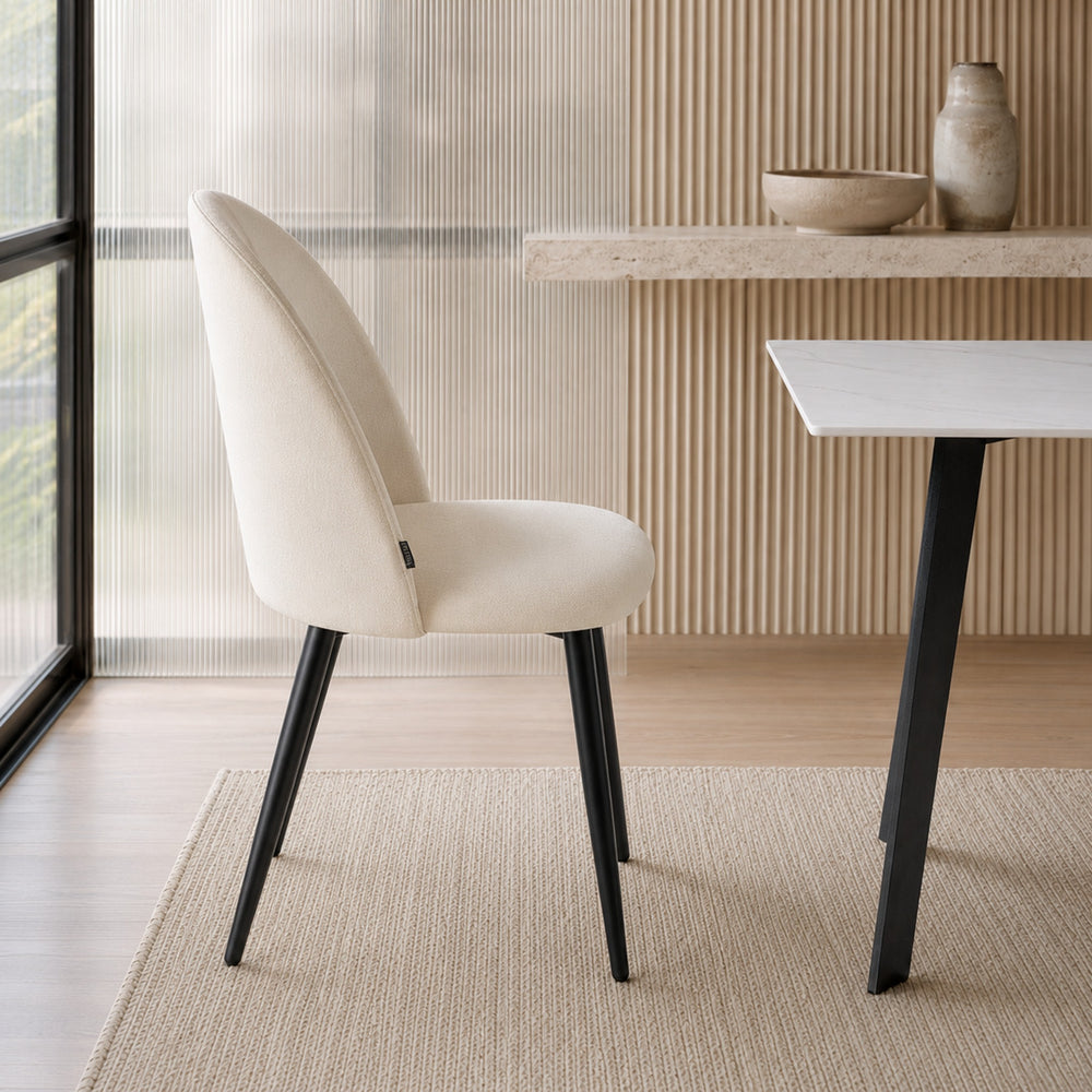 Vista lateral de la silla Livia Lisa beige, resaltando el perfil ergonómico del respaldo y base negra.