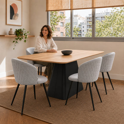Comedor ambientado con sillas Jade tapizadas en pana gris claro y base negra rodeando una mesa de madera clara.