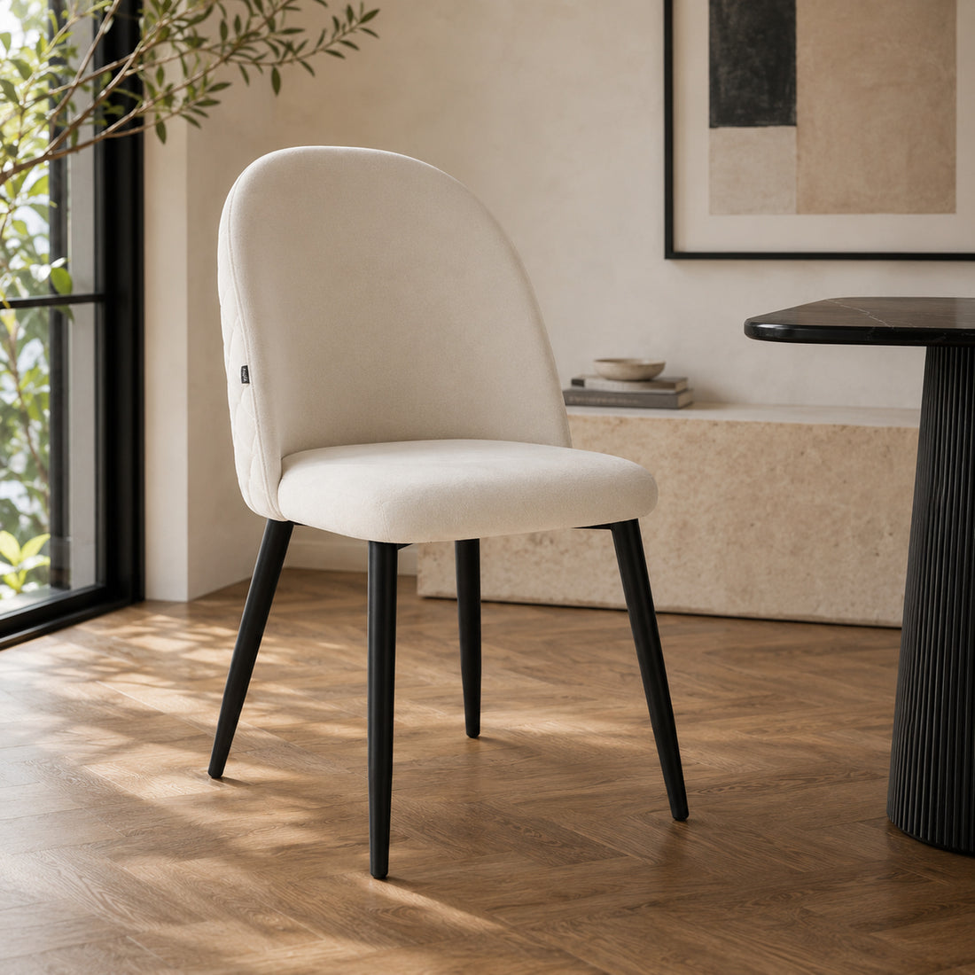 Silla Livia tapizada en pana beige con base metálica negra, vista frontal en tres cuartos.