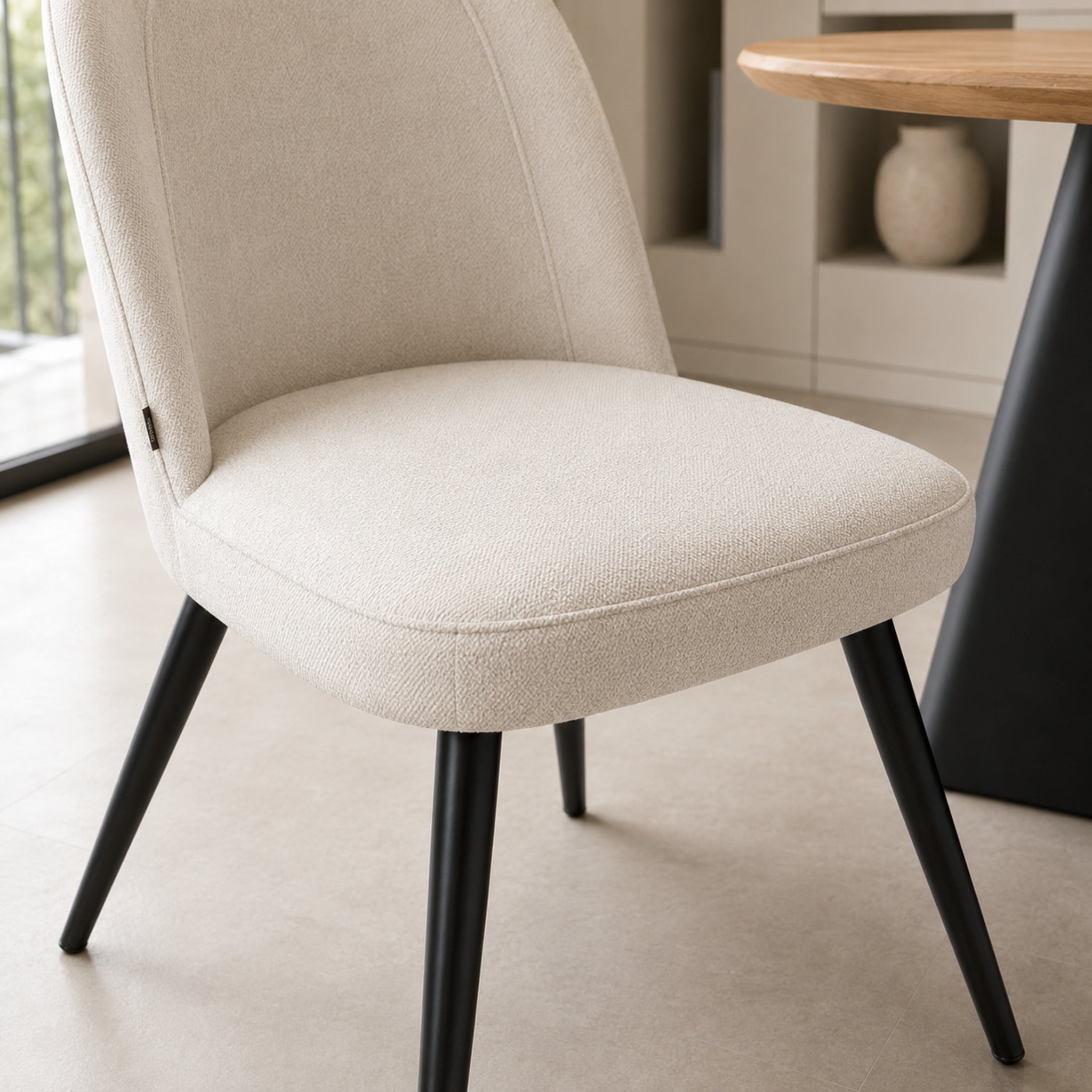 Detalle del asiento acolchado de la silla Lara beige y la unión con las patas metálicas negras.