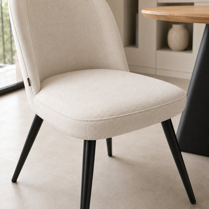 Detalle del asiento acolchado de la silla Lara beige y la unión con las patas metálicas negras.