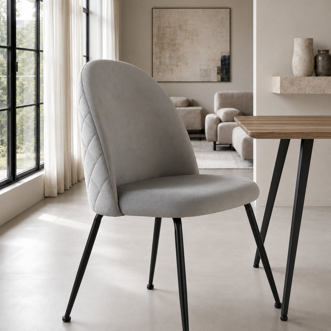 Silla Venecia Matelassé en pana gris claro con base metálica negra, vista frontal junto a una mesa de madera.